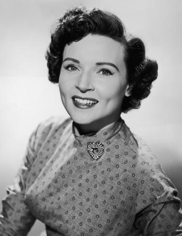 circa 1955:  Promotional studio portrait of American actor Betty White smiling and wearing a patterned dress with a heart-shaped brooch.  (Photo by Hulton Archive/Getty Images)