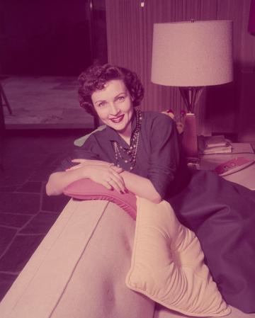 Betty White, US actress and comedian, smiling while sitting with her arms folded across a pillow on the backrest of a sofa in a living room, circa 1955. (Photo by Archive Photos/Getty Images)