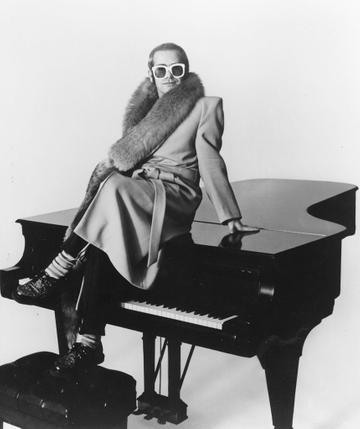 CIRCA 1974:  Pop singer Elton John poses for a portrait sitting on top of a piano wearing a fur-lined coat in circa 1974. (Photo by Michael Ochs Archives/Getty Images)