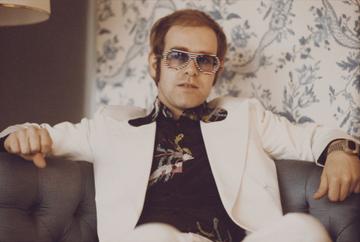 British singer and musician Elton John, wearing a white suit, black shirt with flower motif and multicolored sunglasses, London, November 1973. (Photo by Michael Putland/Getty Images)